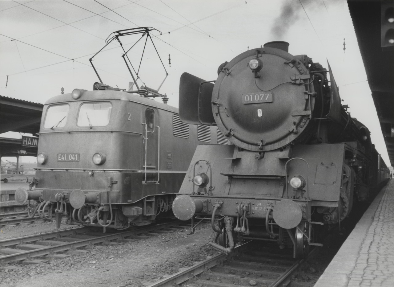 Zwei Einheitslokomotiven, ein ungleiches Paar: Die am Bahnsteig wartende Lok der Baureihe 01 war ein echtes Schwergewicht des Schnellzugdienstes, während die, auf dem Nebengleis stehende, E41 („E“ für elektrisch; später Baureihe 141) die leichteste Ausführung der Einheitselektrolokomotiven war, welche die Dampfloks auf den elektrifizierten Strecken ablösen sollten (Hamm (Westf.) Personenbahnhof, ca. 1965; Westfälischer Heimatbund/Archiv für Alltagskultur, WHB F 2b.9.176)