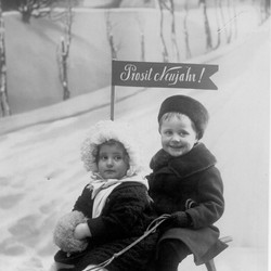 Erna und Wilhelm Tell auf einem Schlitten, versehen mit dem Schriftzug "Prosit Neujahr!" (vergrößerte Bildansicht wird geöffnet)