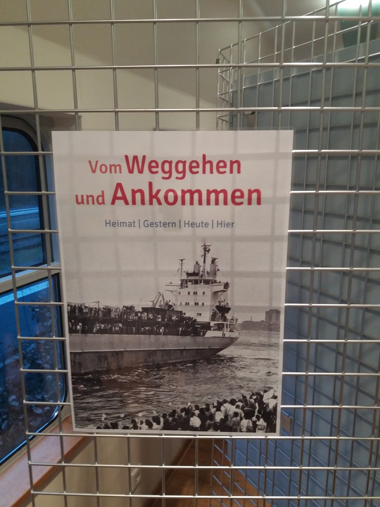Plakat der Ausstellung „Vom Weggehen und Ankommen. Heimat I Gestern I Heute I Hier“.