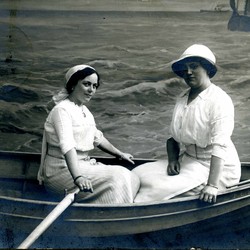 Zwei Frauen in einem Boot, fotografiert vor einem aufwändig gestalteten Hintergrund, der das Meer zeigt. (vergrößerte Bildansicht wird geöffnet)