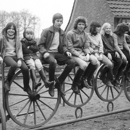 Mehrere Kinder und Jugendliche sitzen auf einem Zaun, neben ihnen steht ein Mann. Foto: Adolf Risse (ca. 1969 - 1979); Archiv für Alltagskultur.