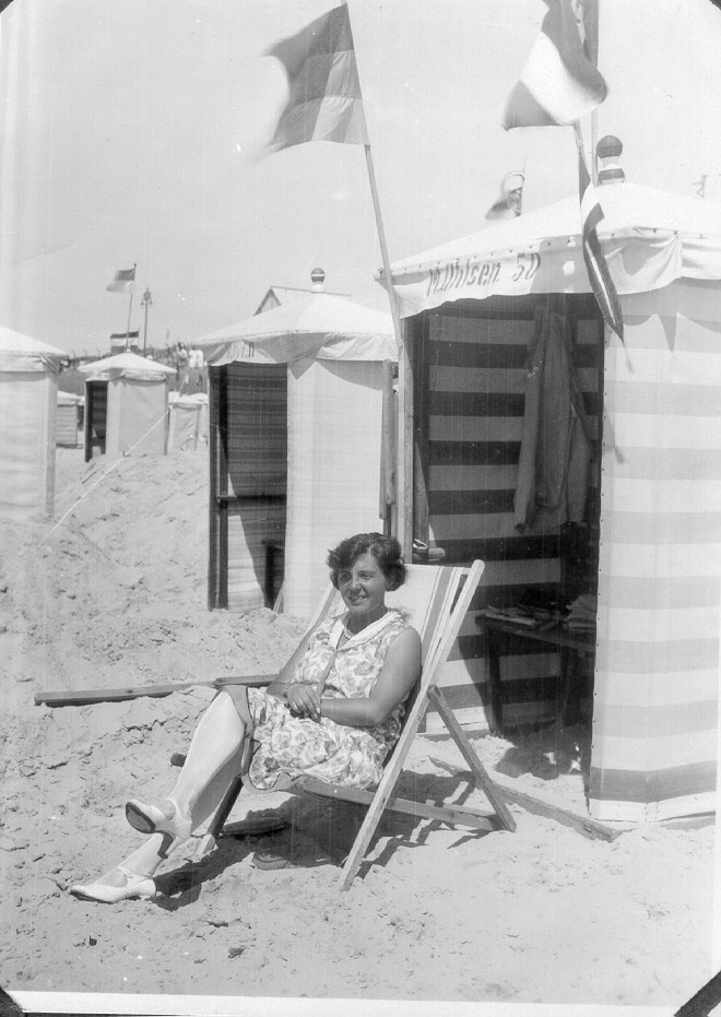 Ein schwarz-weißes Foto einer Frau in einem Strandkorb, an dem zwei Flaggen befestigt sind.