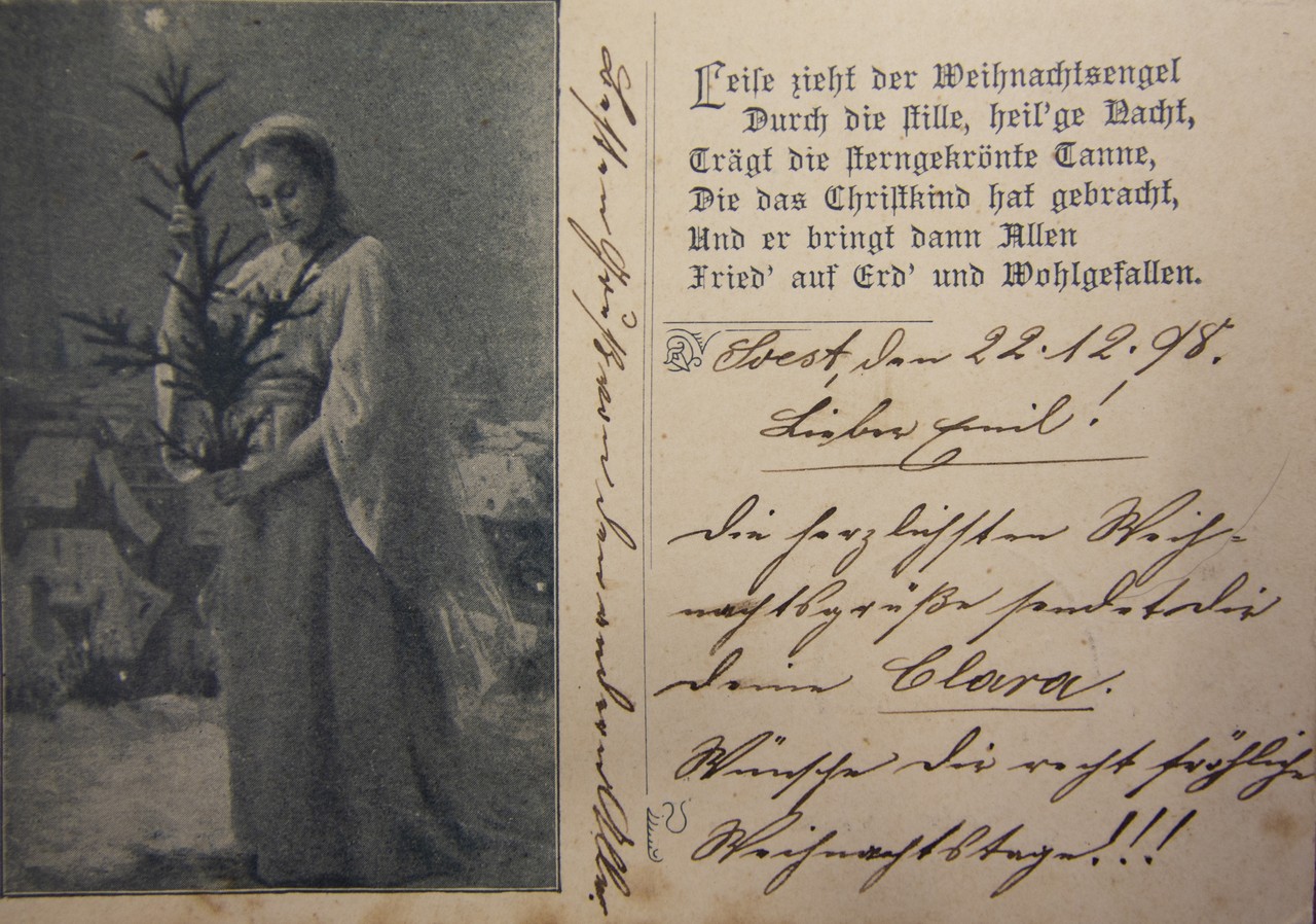 Auf einer ebenfalls an Emil Priebe versandten Weihnachtskarte aus dem Verlag Fritz Grandt, Berlin, die laut Poststempel am 23.12.1898 gelaufen ist, findet sich auf der geteilten Rückseite das s/w-Bild einer Frau mit einem Tannenzweig in Händen vor der Kulisse einer Stadt. Ein auf der linken Seite abgedrucktes sechszeiliges Gedicht erzählt von einem Weihnachtsengel, der  „Fried' auf Erd' und Wohlgefallen“ bringe. Aus dem Text erfahren wir, dass eine Clara aus Soest Emil, der im 5. Infanterie- Regiment Graf Barfuß in Mörchingen, Lothringen, zum Musketier ausgebildet wurde, herzliche Weihnachtsgrüße entrichtet und ihm fröhliche Weihnachtstage wünscht. Foto: Christiane Cantauw, KAF.