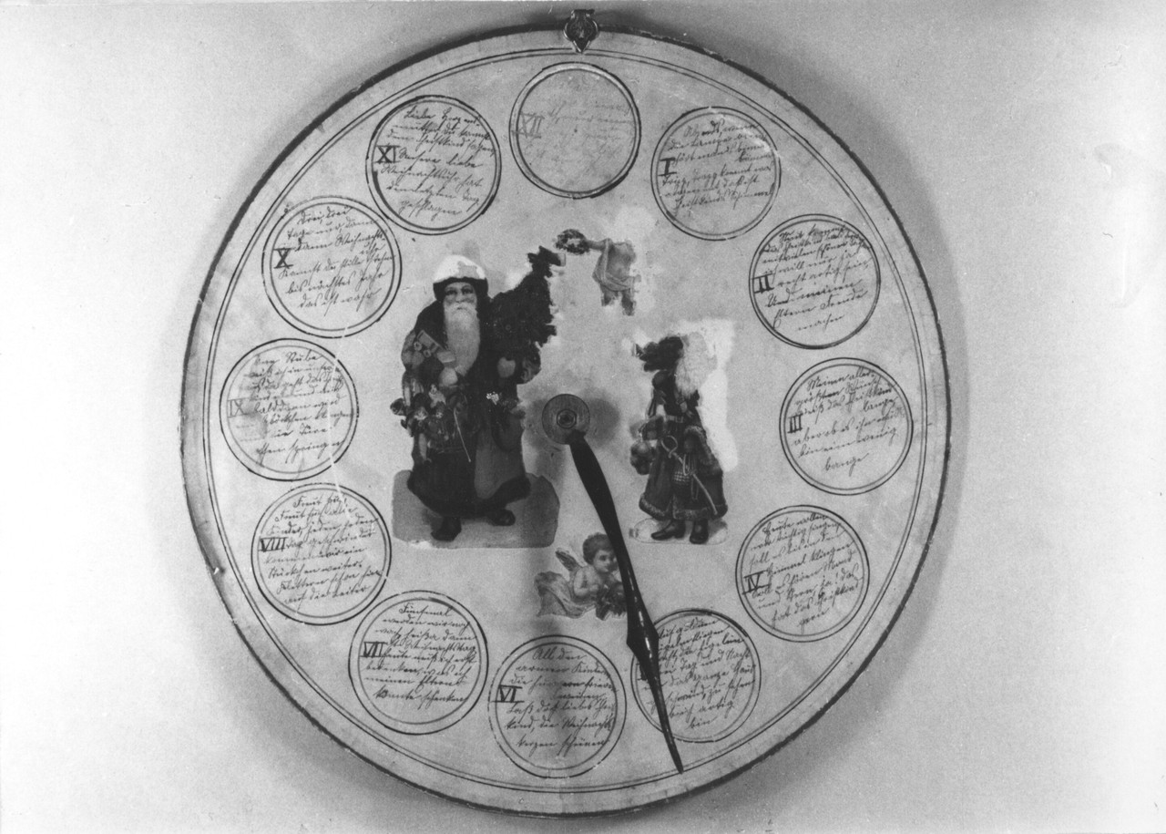 Fotografie einer Weihnachtsuhr von 1926 aus Obermassen, Kreis Unna. Geschenk einer Tante, die die Uhr nach einem Vorbild, das aus der Schweiz stammt, hergestellt hat (Durchmesser 29,5 cm, Papier auf Pappe, Kreise: schwarze und rote Tusche, Glanzbilder, Metallzeiger einer echten Uhr), Archiv für Alltagskultur, Inv.-Nr. 0000.64560.