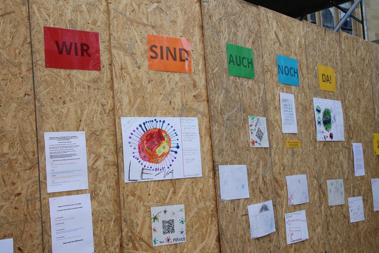 An einem Bauzaun am Münsterschen Dom ist unter dem Titel „Wir sind auch noch da!“ seit dem 24. April eine kleine Freiluftausstellung mit Zeichnungen und Briefen von Kindern zu sehen. Sie dokumentieren, was die Pandemie für sie bedeutet. Foto: Christiane Cantauw, Kommission Alltagskulturforschung.
