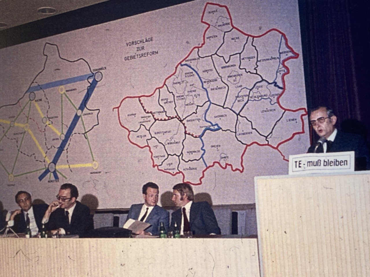 Beim 'Hearing' der Neugliederungskommission 1972 prangte das Schild 'TE muss bleiben' am Rednerpult (Kreisarchiv Steinfurt).