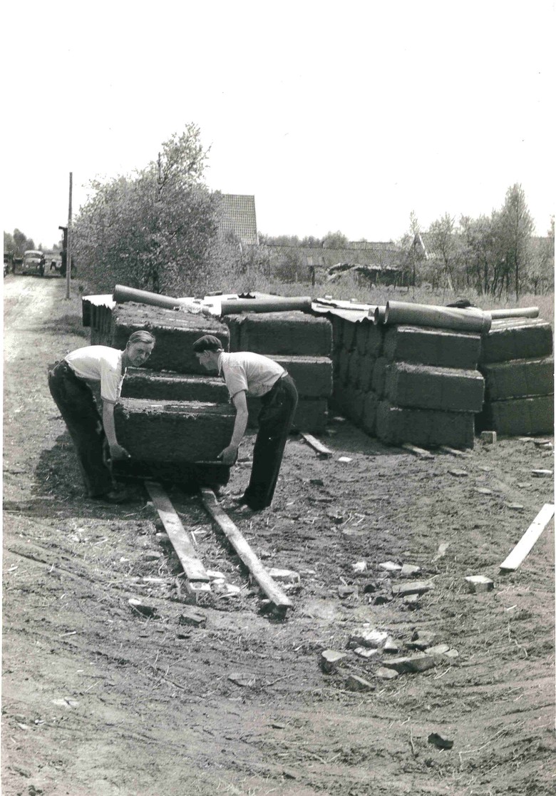 Zwei junge Torfarbeiter stapeln Presstorfballen ab, im Hintergrund ist ein Lastwagen erkennbar. (Foto: STAV Dep. FAHV Nr. 2105z4)