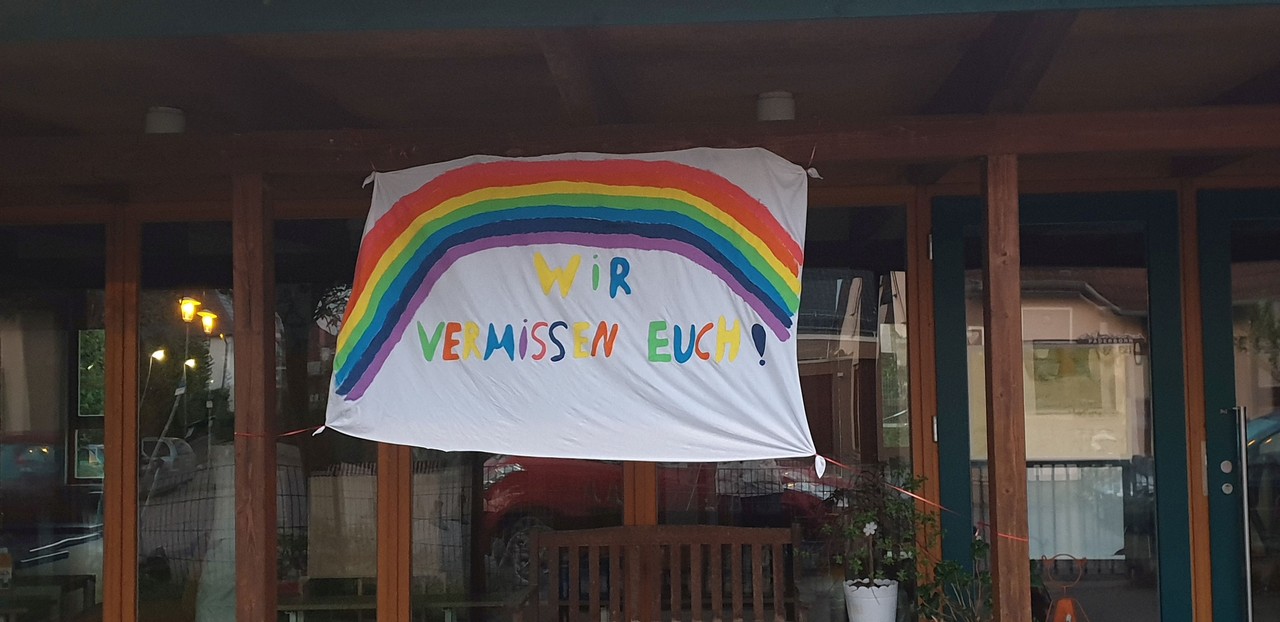 Ein Schild aus Stoff mit einem Regenbogen und der Aufschrift "Wir vermissen euch".
