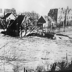 Aus den Fluten der Steinfurter Aa ragt die Niedermühle hervor – im Hintergrund das unerreichbare Krankenhaus. Foto: Stadtmuseum Steinfurt. (vergrößerte Bildansicht wird geöffnet)