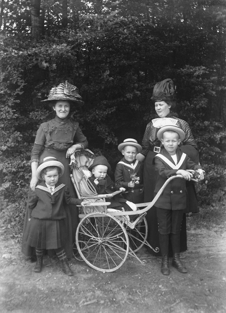 Zwei Frauen und vier Kinder, davon eines im Kinderwagen, die in der Natur fotografiert wurden.