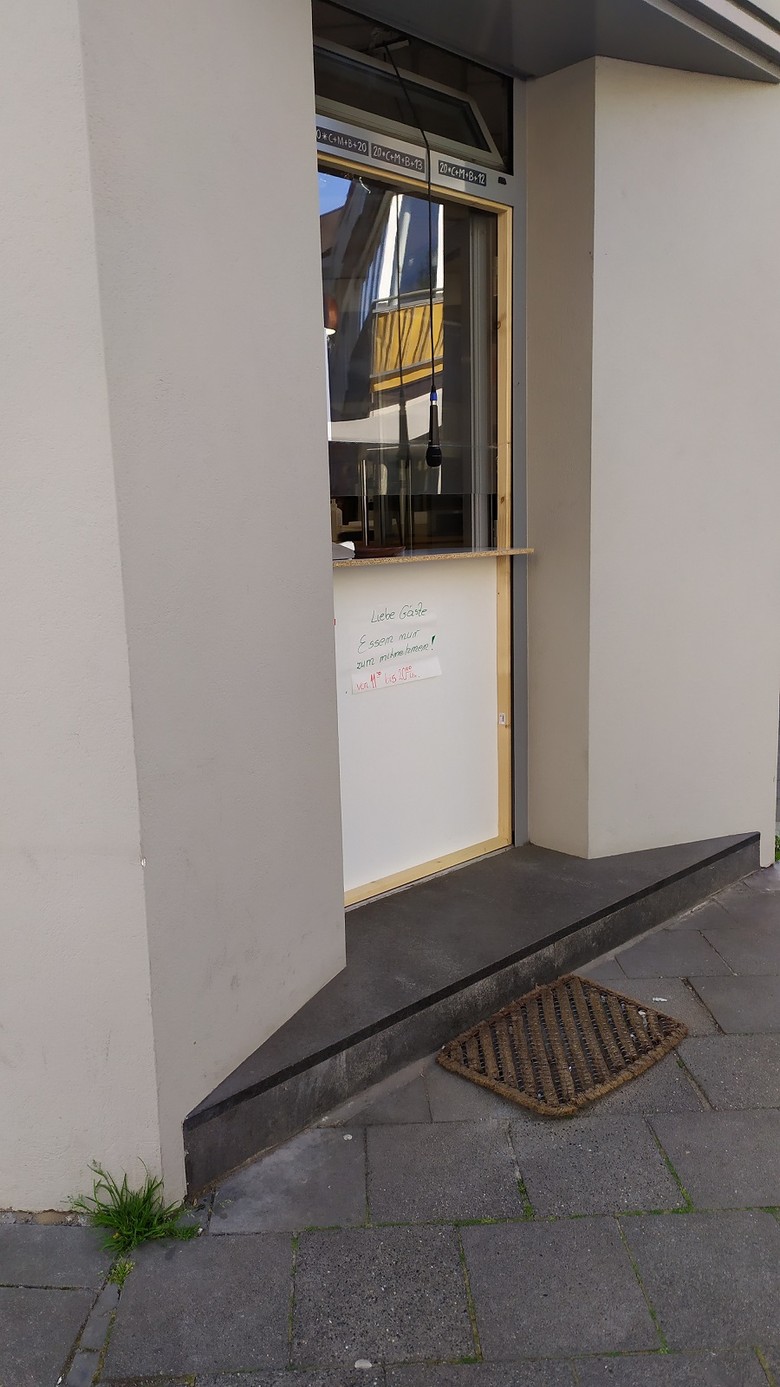 Die Tür eines Lokals wurde durch eine Theke mit Plexiglas ersetzt, aus einem Fenster über der Tür baumelt ein Mikrofon.